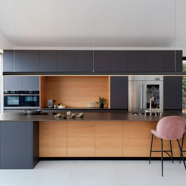 ET2 Continuum linear pendant hung low over a long kitchen island with dark cabinets and pink bar stools