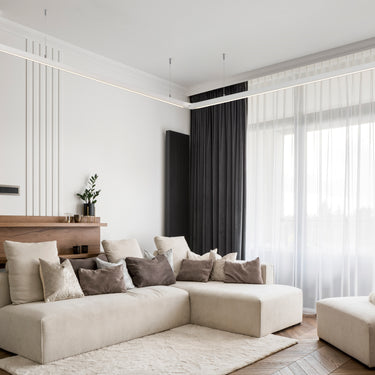 ET2 Continuum linear pendants run along the ceiling of a living room with a cream sectional and sheer curtains