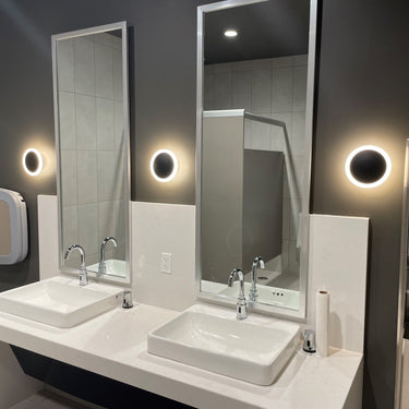ET2 Saucer gold disc wall sconce, three glowing discs beside mirrors over a double-sink restroom vanity