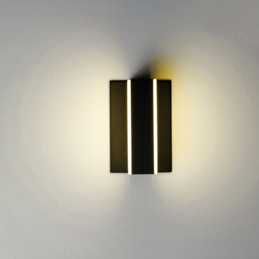 ET2 Omni Black wall sconce lit on a gray wall, light spilling up and down