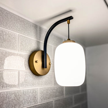 ET2 Soji lantern glass wall sconce with black arm and brass trim on a gray crackle-tile wall, close-up