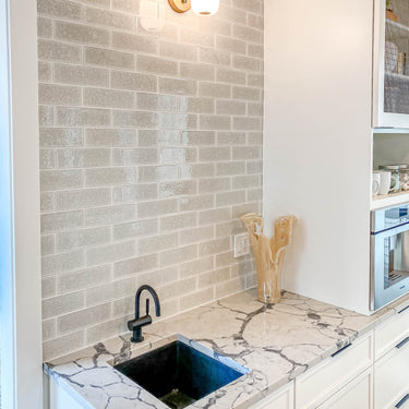 ET2 Soji lantern glass wall sconce on a gray tile wall above a kitchen nook with black sink