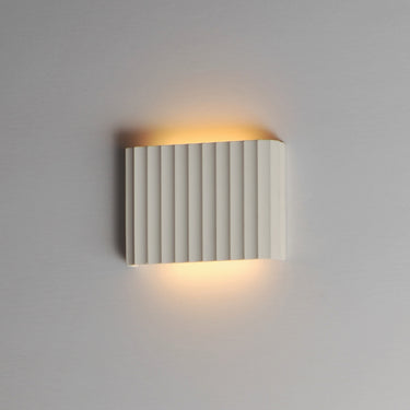 ET2 Delphi fluted concrete wall sconce, Chalk White, lit with warm glow on a gray wall