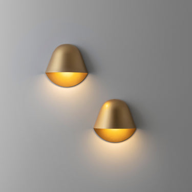 Two matt gold Penta Enoki wall sconces glowing on a wall