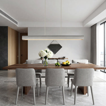 ET2 Matera linear concrete pendant hung over a long wood dining table with gray chairs in a room with tall windows