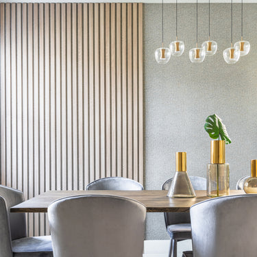 ET2 Newton clear apple glass pendants with brass fonts over a dining table in a room with slatted wood wall