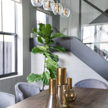 ET2 Newton row of clear apple glass pendants beside a staircase, with brass vases on a wood dining table