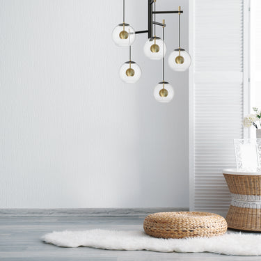 ET2 Nucleus clear glass orb pendant cluster with brass spheres hanging in a bright room beside a rattan stool