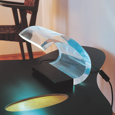 Acrilica table lamp glowing on a dark table with a gold dish