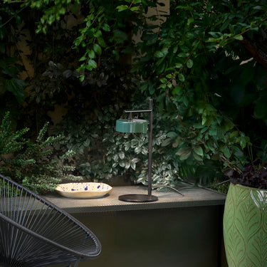 Oluce Berlin-Out table lamp glowing on a garden table at dusk