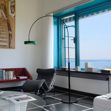 Oluce Berlin-Out arched floor lamp arching over a living room by a sea view window