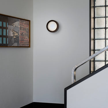 Oluce Berlin-Out round wall lamp on a white wall by a staircase