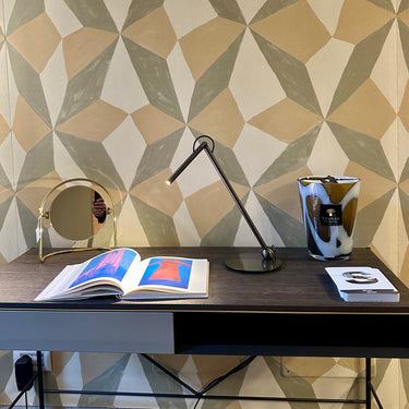 Satin black nickel Oluce Calamaio desk lamp on a console with open magazines and a patterned wall