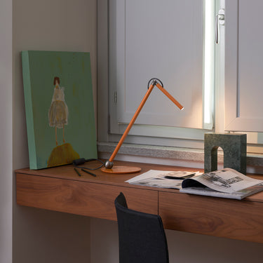 Mustard yellow Oluce Calamaio desk lamp on a walnut desk beside a window