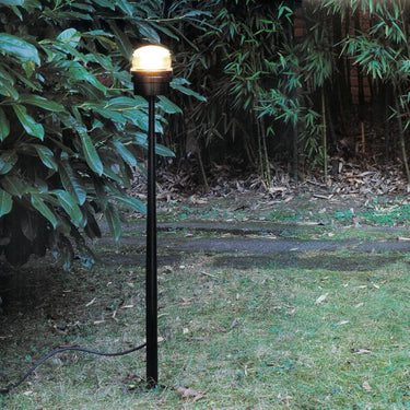 Oluce Fresnel outdoor floor lamp lit in a garden