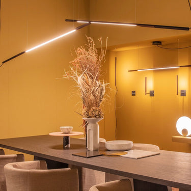 Ilo horizontal LED pendant lighting a dining table in a warm ochre room with dried flowers