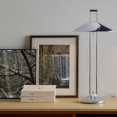 Regina T table lamp in aluminium beside framed art and books on a wooden console
