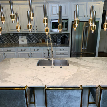 ET2 Reveal tube pendants with gold bands above a marble island and stools in a kitchen (Satin Nickel and Satin Brass version)