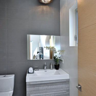 ET2 Sense mirror chrome flush mount on the ceiling of a gray-tiled powder room with a floating wood vanity and mirror