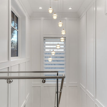 ET2 Swank orb pendants cascading down a white stairwell from a Natural Aged Brass canopy