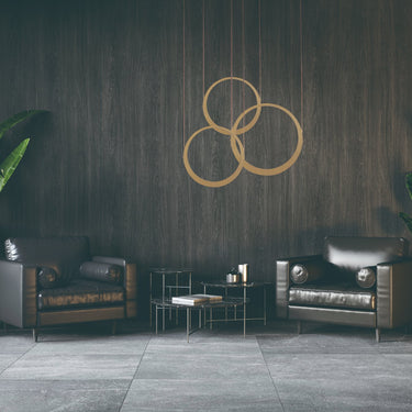 ET2 Tether three overlapping brass leather ring pendants hung on a dark wood wall between two leather armchairs and plants