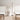 Black Moneta Medium floor lamp between two lounge chairs and a small stool with a vase of branches