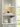 Caspe 6 rechargeable lamp in Bronze glowing on a lit white bookshelf above a stack of books