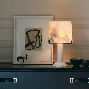 Acropolis table lamp lit on a navy console in front of framed abstract art