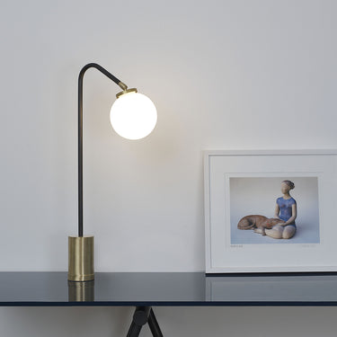 Array table lamp in bronze with a lit opal glass globe on a side table in a room