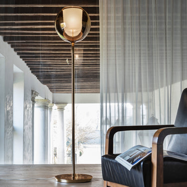 Penta Glo floor lamp, a glass sphere on a slim metal stand, lit in a living room