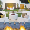 Two white Check lounge chairs flanking a round white ottoman beside a fire pit in a courtyard garden