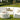 Curved white modular sectional with a round ottoman and pillows on a formal garden lawn