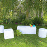 White Dot cylinder and cube ottomans with a Dash bench on a lawn with colorful cups