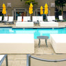 Two white Play Pad resort beds on a pool deck beside lounge chairs and an umbrella table