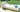 White Surf sun lounge with a pillow and a rolled turquoise towel on a stone patio beside a lawn