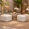 Two Zest corner ottomans in white vinyl beside a stone pedestal table in a candlelit spa courtyard