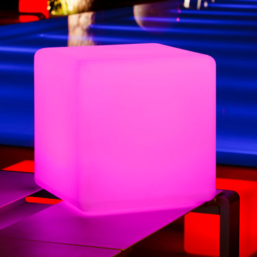 Magenta glowing Cube lamp on a dark table with blue and red lighting behind it