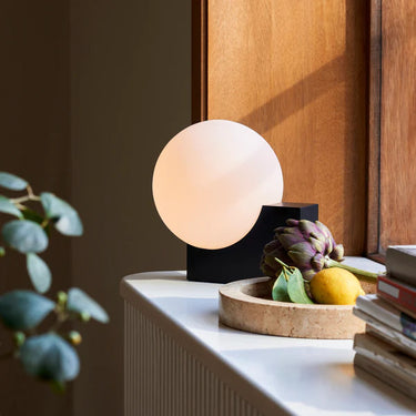 &Tradition Journey bedside lamp, black finish, casting warm ambient light in a contemporary bedroom. 