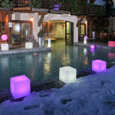 Purple and white glowing Cube lamps spaced along a pool edge at dusk